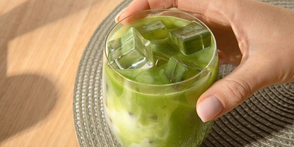 Hand hält Iced Matcha mit Ice Cubes