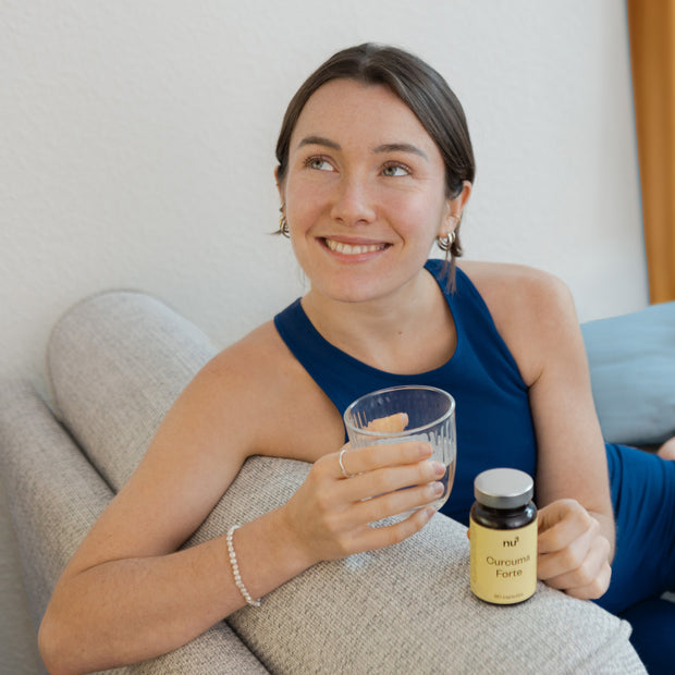 Frau auf dem Sofa mit Kapseln und Glas Wasser